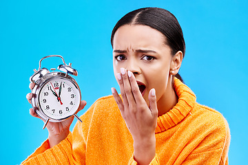 Image showing Portrait, surprise and woman with an alarm clock, late and deadline with girl against a blue studio background. Face, female model and person with time, shocked and stress with schedule and wow