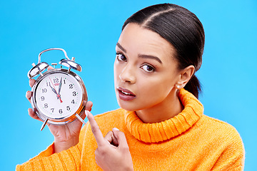 Image showing Woman, annoyed and point at alarm clock in portrait for warning by blue background in studio. Gen z girl, student and model with watch, time management and schedule with angry face to start morning