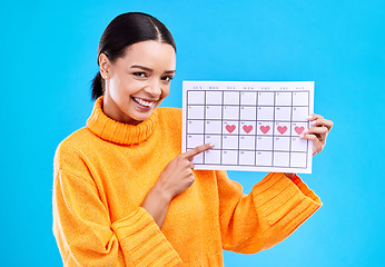 Image showing Health, portrait and female with a calendar in a studio to track her menstrual or ovulation cycle. Happy, smile and face of a woman model pointing to a paper period chart isolated by blue background.