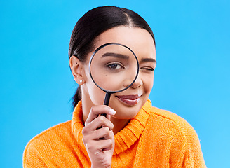 Image showing Search, portrait and female with a magnifying glass in a studio for an investigation or detective cosplay. Happy, smile and headshot of a woman model with a zoom magnifier isolated by blue background