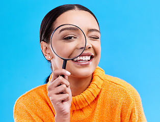 Image showing Happy, portrait and female with a magnifying glass in a studio for an investigation or detective cosplay. Happiness, smile and headshot of a female model with a magnifier isolated by blue background.