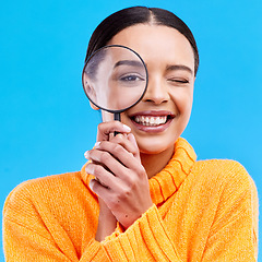 Image showing Smile, portrait and woman with a magnifier in a studio for an investigation or detective cosplay. Happiness, excited and headshot of a female model with a magnifying glass isolated by blue background