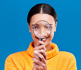 Image showing Woman, magnifying glass and smile in studio portrait with funny face, search and zoom by blue background. Gen z girl, investigation and research with lens for study, inspection and check by backdrop