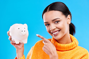 Image showing Happy woman, money and pointing to piggy bank for investment, budget or finance against blue studio background. Portrait of female with savings, cash or coin for profit investing or financial freedom
