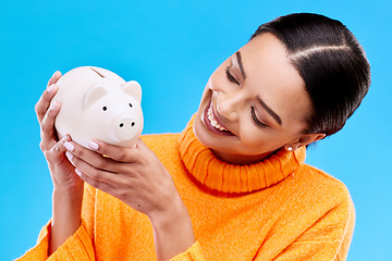 Image showing Happy woman, money and piggy bank for investment, budget or finance against a blue studio background. Female smile holding savings of cash or coin for change, profit or investing in financial freedom