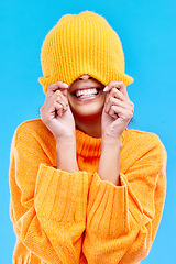 Image showing Fashion, crazy and cover with woman and beanie in studio for hiding, winter and goofy. Playful, happiness and smile with female and knitted hat isolated on blue background for funny, silly and cool