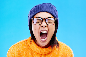 Image showing Portrait of woman in winter fashion, screaming with beanie and glasses isolated on blue background. Anger, frustration and face of frustrated gen z girl in studio with warm clothes for cold weather.