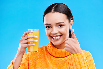 Image showing Happy woman, portrait and thumbs up for orange juice in studio, blue background and yes emoji. Female model, drinking glass and good review of fruit cocktail for nutrition, vitamin c diet and detox