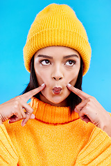 Image showing Goofy woman in winter fashion with comic expression, beanie and fun isolated on blue background. Style, happiness and silly gen z girl in studio with funny face and warm clothing for cold weather.