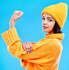 Image showing Portrait of woman in winter fashion with power, beanie and glasses isolated on blue background. Style, arm flex and gen z girl in studio backdrop with strong face and warm clothing for cold weather.