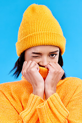 Image showing Portrait of woman in winter fashion with cozy jersey, beanie and wink isolated on blue background. Style, happiness and gen z girl in studio backdrop with mock up and warm clothing for cold weather.