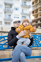 Image showing Young mother with her cute infant baby boy child on bench in city park.