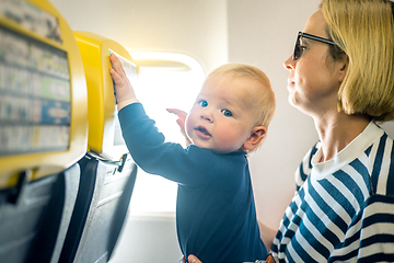 Image showing Mom and child flying by plane. Mother holding and playing with her infant baby boy child in her lap during economy comercial flight. Concept photo of air travel with baby. Real people.