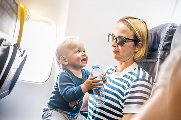 Image showing Mom and child flying by plane. Mother holding and playing with her infant baby boy child in her lap during economy comercial flight. Concept photo of air travel with baby. Real people.