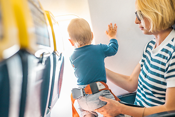 Image showing Mom and child flying by plane. Mother holding and playing with her infant baby boy child in her lap during economy comercial flight. Concept photo of air travel with baby. Real people.