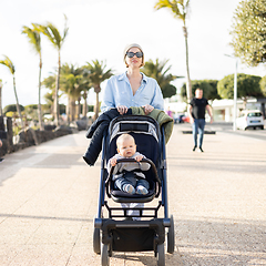 Image showing Young mother walking and pushing her infant boy child in baby stroller along palm lined beach promenade of Puerto del Carmen, Lanzarote, Canary islands, Spain