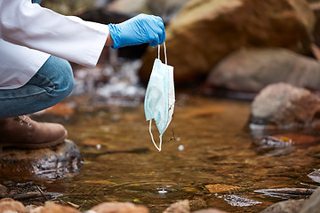 Image showing Pollution, litter and face mask in river with hand of person for nature conservation, environment and safety. Covid, danger and trash with garbage in water for medical waste, healthcare and cleaning