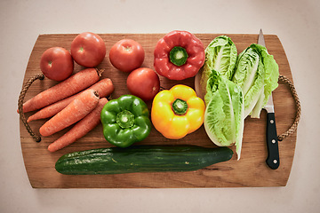 Image showing Vegetables, cutting board and healthy food on the counter in the kitchen for a vegan meal. Crops, wood and diet with fresh, organic and natural produce with a knife for cooking a vegetarian dinner.