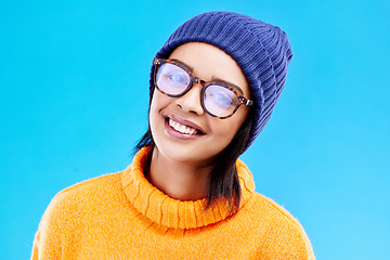Image showing Portrait of happy woman in winter fashion with glasses, beanie and smile isolated on blue background. Style, happiness and face of gen z girl on studio backdrop with warm clothing for cold weather.