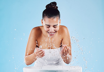 Image showing Sink, water splash and happy skincare of a woman washing face for natural beauty and facial wellness. Isolated, blue background and studio with a female model doing dermatology and cosmetic routine