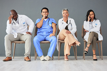 Image showing Tired, team and doctors waiting in the hospital with frustration, sad and burnout. Yawn, people and group of stressed professional healthcare workers sitting in a line in hallway in a medical clinic.