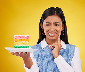 Image showing Upset woman, rainbow cake and studio while thinking of birthday celebration, disaster or mistake. Face of Indian gen z female with dessert food with color, foul smell or bad idea on yellow background
