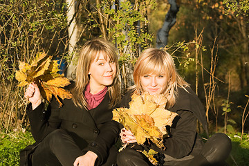 Image showing Two young women with autumn leaves in park