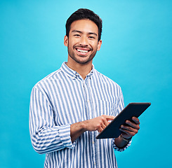 Image showing Tablet, Asian man and smile portrait in a studio on social media, internet and website app scroll. Happiness, isolated and blue background with a male model reading technology for digital networking