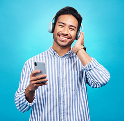 Image showing Happy man in portrait, smartphone and headphones, listen to music with entertainment on blue background. Male person with smile, wireless technology and online audio streaming with radio or podcast