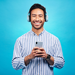 Image showing Music, headphones and happy man with phone in studio for streaming, audio and subscription against blue background. Radio, smile and face of asian male online for podcast, track and internet app