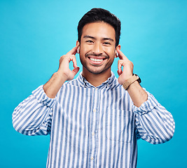 Image showing Portrait, earphones and happy man with music in studio, relax and smile on blue background. Radio, face and asian male listening to podcast, streaming or audio, online or subscription while isolated