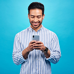 Image showing Happy man, smartphone and earphones, music and social media with entertainment and chat on blue background. Male person with smile, wireless technology and online audio streaming with texting on app