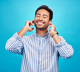 Image showing Happy man, earphones and and music in studio, relax and cheerful on blue background. Radio, smile and indian male smile while listening to podcast, streaming or audio, online or subscription isolated