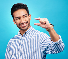 Image showing Small, hand and gesture of a man with a smile in studio showing a tiny measurement. Isolated, blue background and male model show happiness and positive opinion with hands from small size sign