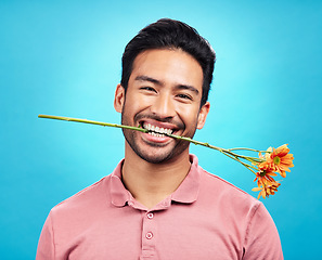 Image showing Teeth, flower and portrait of man in studio for celebration, gift and romance. Funny, goofy and present with male isolated on blue background for happiness, smile and valentines day mockup