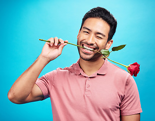 Image showing Teeth, rose and wink with portrait of man in studio for celebration, gift and romance. Funny, goofy and present with male and flower on blue background for happiness, smile and valentines day mockup