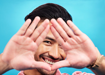 Image showing Frame, hands and portrait of happy Asian man on blue background with smile, confidence and happiness. Perspective, shape and face of male person in studio for photography, profile picture and vision