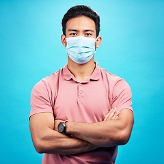 Image showing Man in face mask, arms crossed in portrait and covid, safety from virus, bacteria and germs isolated on blue background. Disease, corona and male person, health compliance with protection in studio