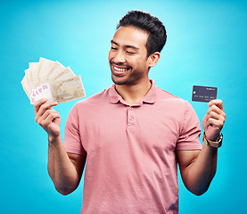 Image showing Credit card, smile and money by happy man in studio with savings, finance or investment growth on blue background. Cash, profit and asian guy excited for banking, loan or financial freedom isolated