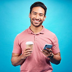 Image showing Earphones, coffee and portrait of man with phone in studio isolated on a blue background. Tea, cellphone and happiness of Asian person with drink, caffeine and mobile for social media, music or radio