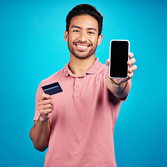 Image showing Portrait, phone and credit card for online shopping with a man customer on a blue background in studio. Happy, smile and ecommerce with a young shopper using fintech to make a payment or transaction