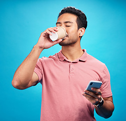 Image showing Earphones, drinking coffee and man with phone in studio isolated on a blue background. Tea, cellphone and Asian person drink, caffeine or espresso with mobile for social media, radio music or podcast
