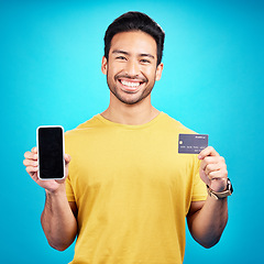 Image showing Portrait, phone and credit card for ecommerce with a man customer on a blue background in studio. Happy, smile and online shopping with a young shopper using fintech to make a payment or transaction