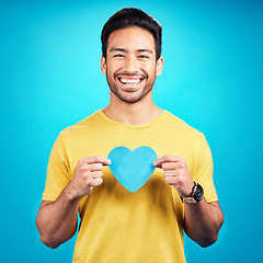 Image showing Portrait, cutout heart and Asian man with happiness, loving and emoji with guy against a blue studio background. Face, male person and model with symbol for love, smile and carefree with support