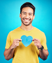Image showing Portrait, cutout heart and Asian man with support, wellness and confident person against blue studio background. Face, male model or guy with symbol for love, cheerful and emoji with smile and loving
