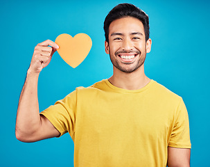 Image showing Portrait, cutout heart and Asian man with smile, support and loving against blue studio background. Face, male person and model with symbol for love, happiness and emoji with wellness and confident