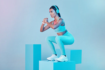 Image showing Fitness, squat and woman with focus, exercise and confident person against blue studio background. Female, model and athlete with headphones, workout goal or balance for wellness or healthy lifestyle