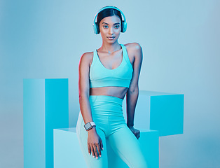 Image showing Portrait, fitness and woman with headphones, exercise and confident girl against a blue studio background. Face, female model and person with headset, inspiration and streaming music for workout goal