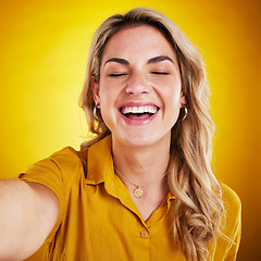 Image showing Selfie, face and smile with a laughing woman on a yellow background in studio for fun or humor. Eye closed, comic and funny with an attractive young female model enjoying comedy, being silly or goofy