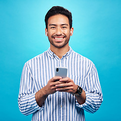 Image showing Happy, portrait and a man with a phone for communication isolated on a blue background in a studio. Smile, social media update and a person typing on a mobile for app, notification reply and message